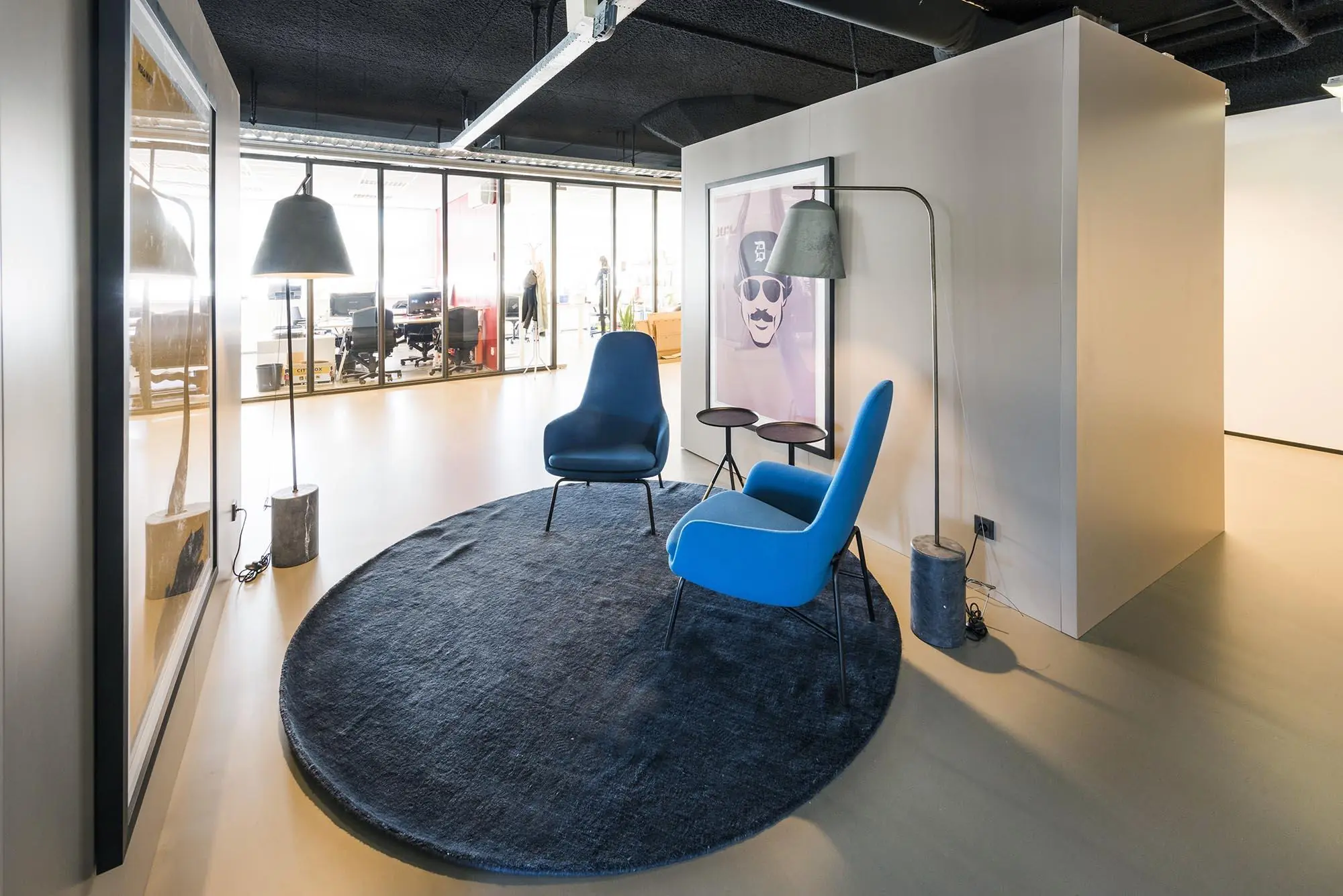 Moderne zithoek met twee blauwe stoelen, een donkerblauw rond vloerkleed en staande lampen in een kantoor aan de Anthony Fokkerweg.